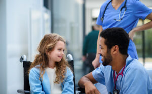Young doctor talking to a little girl in a wheelchair
